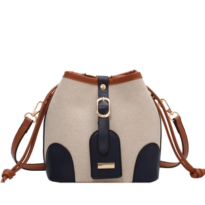 Canvas bucket bag with blue leather patchwork and brown shoulder strap on white backdrop