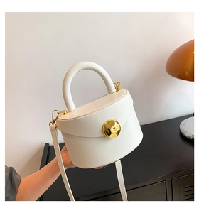 Detail of a white structured handbag featuring a round gold clasp and minimalist leather handle