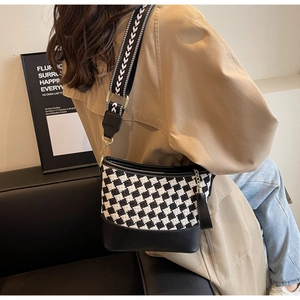 Detail of checkered bucket bag with wide geometric strap worn by model in a chic room