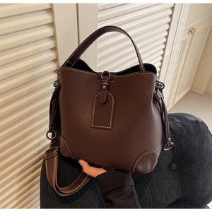 Detail der tiefbraunen Beuteltasche mit Litschi-Leder und gestreiftem breitem Schultergurt