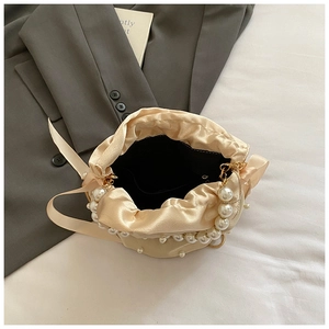 Close-up of champagne satin bucket bag featuring pearl handle and ribbon detail