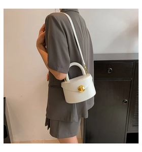 Detail of white semi-circular handbag with golden circular lock and fixed top handle