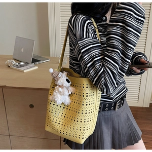 Close-up of bright yellow hollow out bucket bag with a cute white puppy bag charm