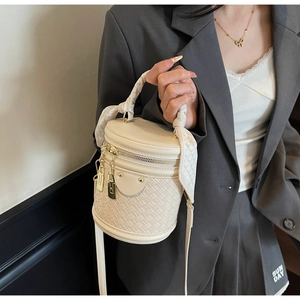 Detail of cream bucket bag with woven texture, silk scarf handle, and gold lock charms
