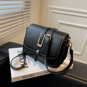 Classic black leather square shoulder bag with gold metal buckle on white books background
