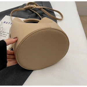 Dettaglio della borsa a secchiello beige con trama a grana e fibbie in metallo dorato lucido
