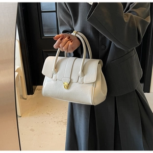 Detail of cream white leather handbag with golden metal buckle and top handle design
