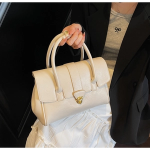 Detail of cream white leather handbag featuring gold twist lock and elegant top handles