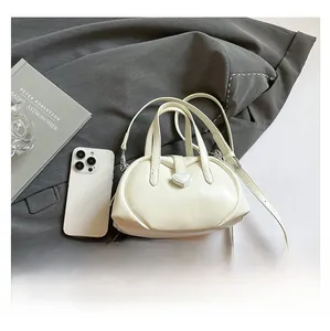 Detailed top view of a cream leather shell bag with heart clasp on grey fabric background