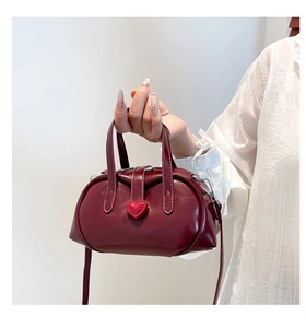 Detail of burgundy mini shell handbag with a 3D red heart buckle and polished texture
