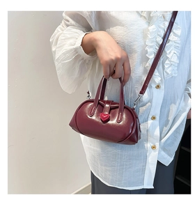 Detail of burgundy mini handbag with red heart buckle worn by model showing size and scale