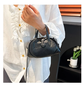 Detail of a black glossy leather shell bag with a gold heart-shaped buckle for commuting