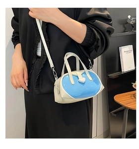 Close-up of a blue and cream contrast shell crossbody bag with heart detail worn by a model