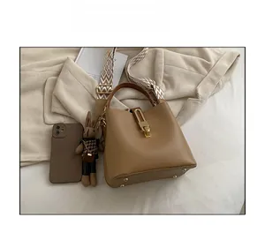 Detail of a brown bucket bag featuring a wide geometric strap and golden hardware accents