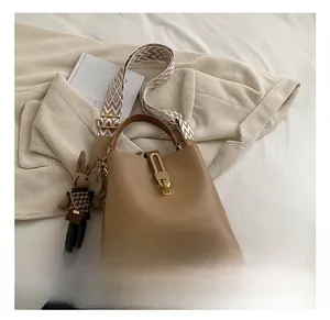 Detail of brown leather bucket bag featuring wide geometric strap and rabbit charm decor