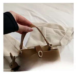 Close-up of khaki leather bucket bag with golden buckle and knit rabbit charm