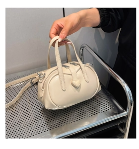 Detail of a creamy white mini bowling bag featuring a heart-shaped design and dual zippers