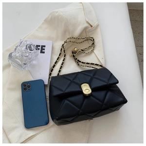 Detail of black quilted leather chain bag with golden oval twist lock on a beige blazer