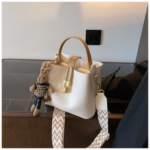 Detail of cream bucket bag featuring wide woven strap and golden U-shaped metal lock