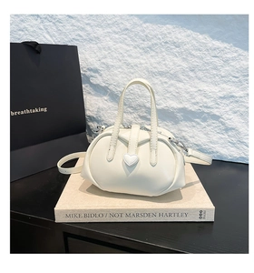 Close-up of cream white handbag featuring a distinctive white heart-shaped clasp detail