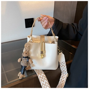 Detail of white leather bucket bag with gold clasp and geometric strap with rabbit charm