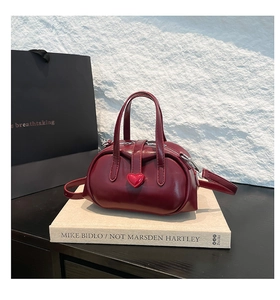 Close-up of retro burgundy glossy leather bag with heart ornament on a book