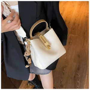 White PU bucket bag with wide geometric strap and brown handle held by a model