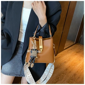 Close-up of brown bucket bag with wide woven strap and rabbit plush pendant detail