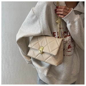 Detail of beige quilted crossbody bag with gold chain strap and oval lock on a model