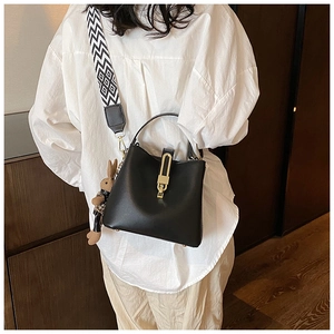 Detail of black bucket bag featuring a geometric wide strap and cute rabbit pendant