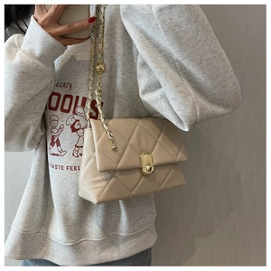 Close-up of beige quilted crossbody bag with gold chain strap and oval metal lock