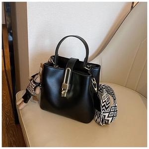 Detail of black leather bucket bag with gold lock buckle and geometric wide strap