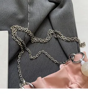 Detail of pink pleated bag featuring long silver metal chain and marble bead charm