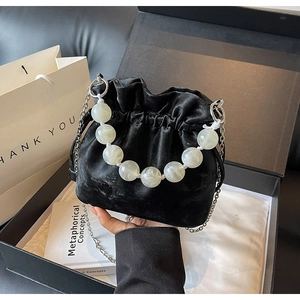 Detail of a black velvet drawstring bucket bag with marble beads handle in a gift box