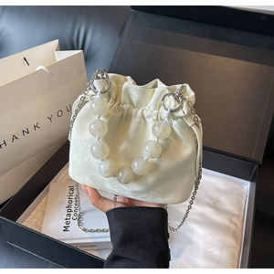 Detail of off-white satin drawstring bucket bag with pearl handle and silver chain