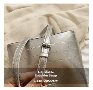 Detail of adjustable silver shoulder strap with metallic buckle on textured bucket bag