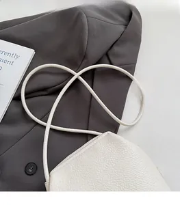 Detail of white lychee leather handbag with slim shoulder strap on a grey suit jacket