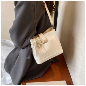 Detail of cream bucket bag with crocodile pattern and pearl bow charm on shoulder