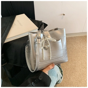 Detailed shot of silver bucket bag with crocodile embossing and pearl bow charm accessory