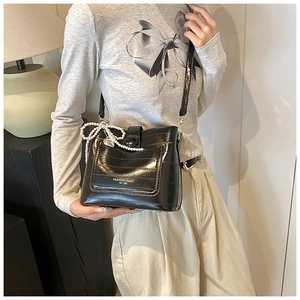 Detail of black crossbody bag with crocodile texture, pearl bow charm, and metal accents