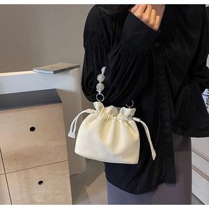Detail of off-white pleated bucket bag with decorative pearl bead handle and drawstring