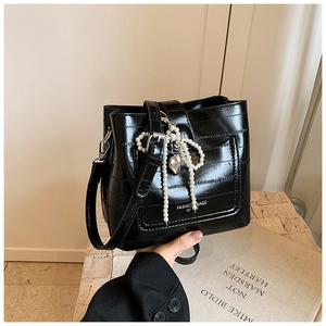 Detail of black crocodile embossed bucket bag featuring a pearl bow and silver heart charm
