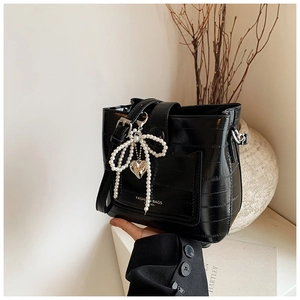 Detail of black crocodile pattern handbag with pearl bow charm and silver heart pendant