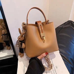 Chic brown bucket bag with wide woven strap and cute bunny pendant on white books