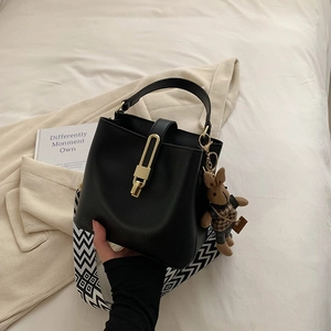 Solid color bucket bag with wide geometric strap and rabbit charm in black leather
