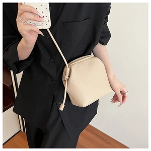Detail showing the lychee grain texture and side knot of the cream faux leather crossbody bag