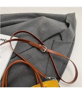Détail de la bandoulière réglable en cuir marron avec boucle argentée sur sac en toile jaune