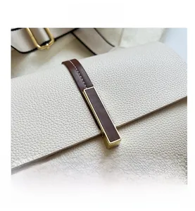 Detail shot of the textured cream leather crossbody bag with a gold buckle and brown strap