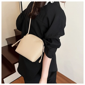 Side view of beige lychee texture PU leather shoulder bag worn by model on stairs