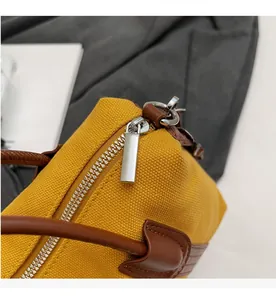 Détail de la fermeture éclair argentée et garniture en cuir brun sur un sac en toile jaune